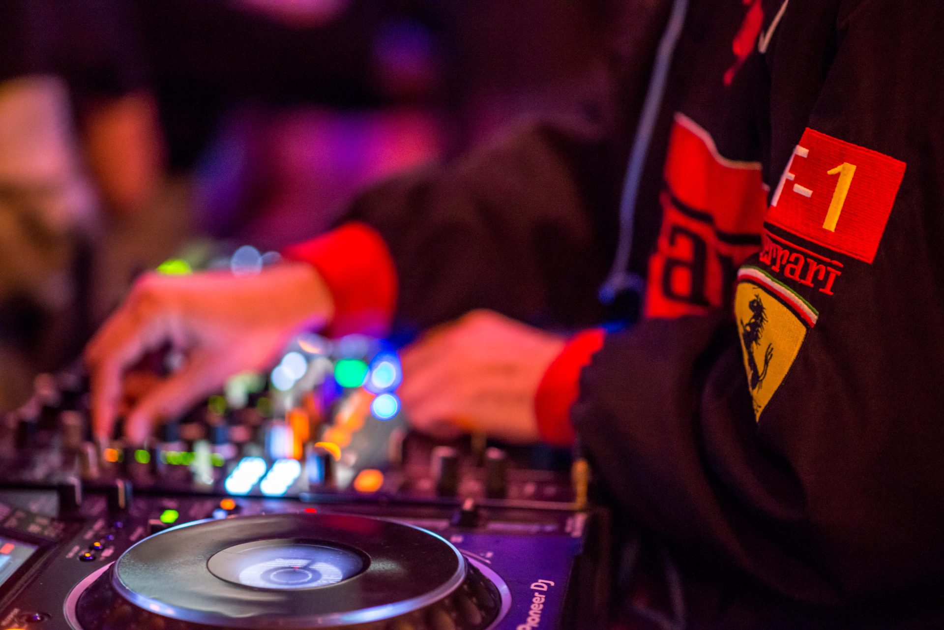 DJ spielt an einem Mischpult, umgeben von buntem Licht und einer lebhaften Atmosphäre.