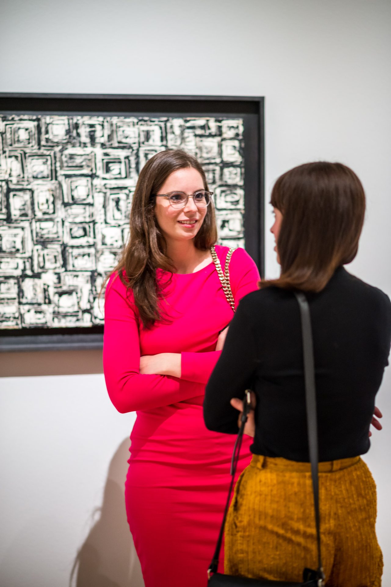 Zwei Frauen unterhalten sich in einer Kunstgalerie vor einem zeitgenössischen Kunstwerk.
