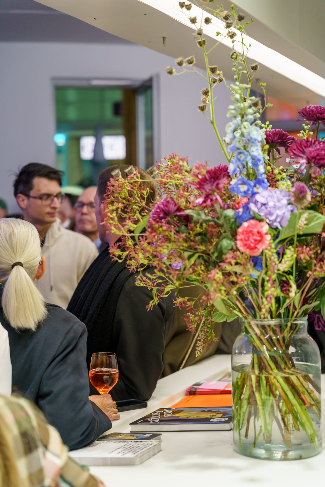 Blumenarrangement auf einer Theke mit Gästen im Hintergrund, die eine einladende Atmosphäre schaffen.