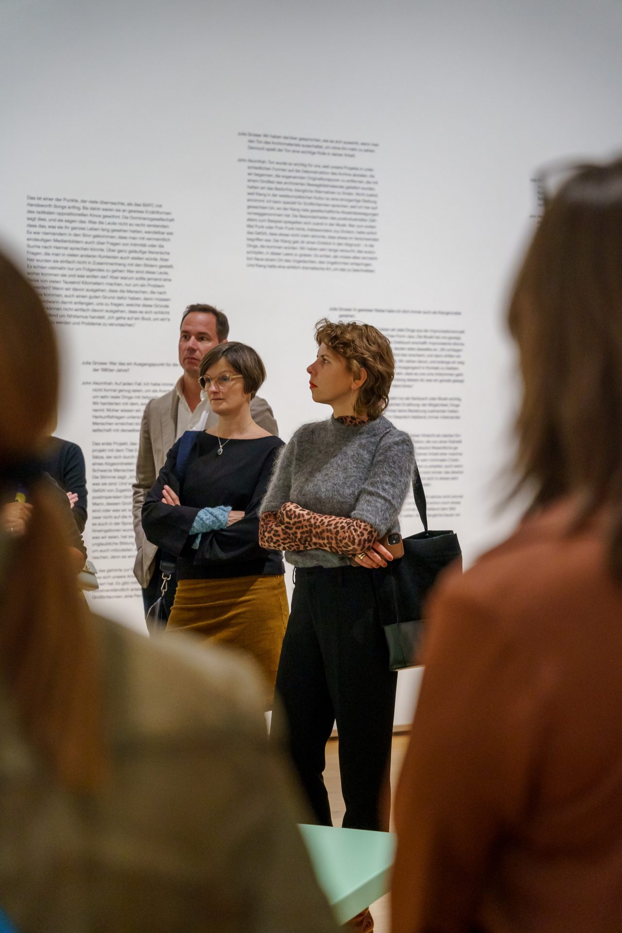 Museumsgäste betrachten eine Ausstellung, während im Hintergrund Texte an der Wand zu sehen sind.