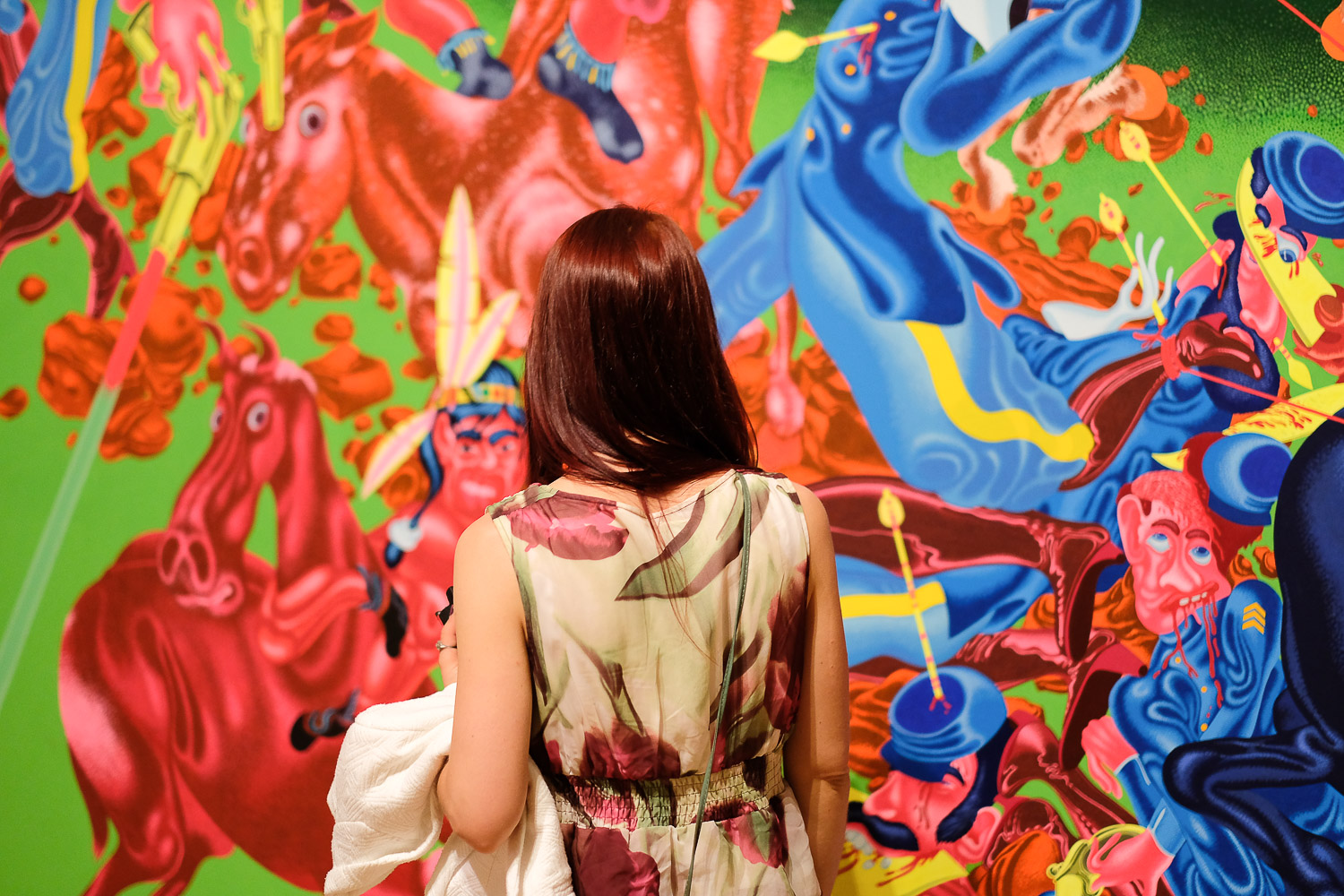 Eine Person betrachtet ein lebhaftes, farbenfrohes Wandgemälde mit Pferden und Figuren.