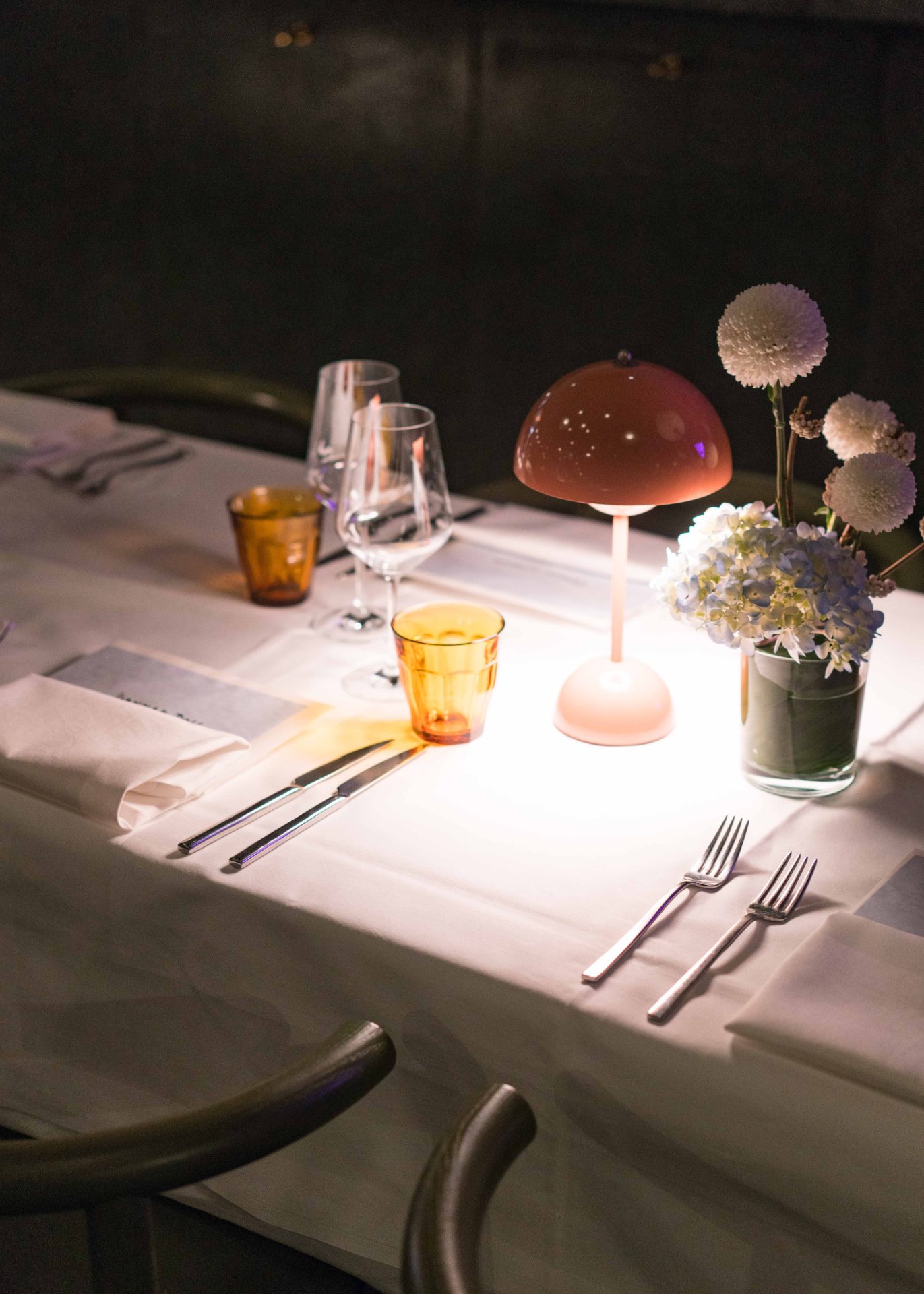 Tisch gedeckt mit Gläsern, Besteck, einer Lampe und Blumen in einer behaglichen Atmosphäre.