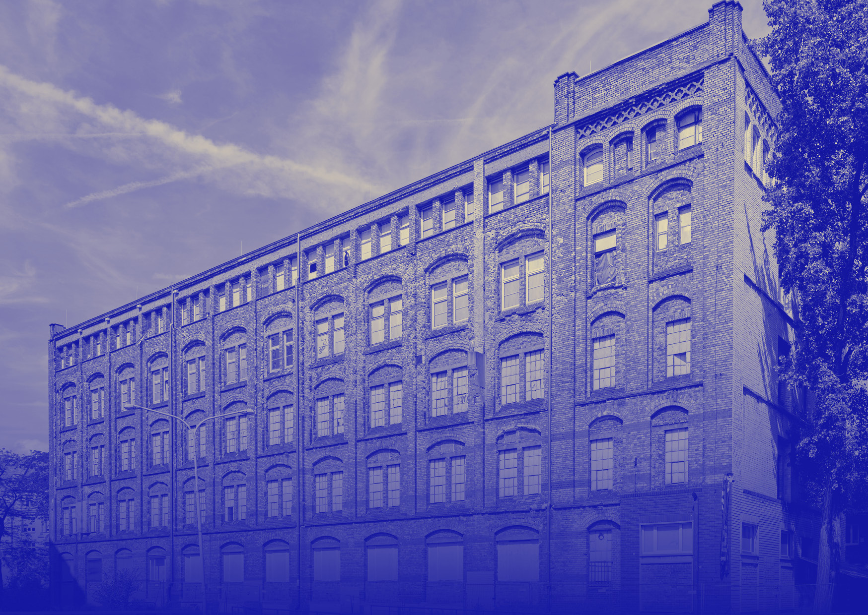 Historisches Ziegelgebäude mit vielen Fenstern vor klarem Himmel, blau gefiltert.