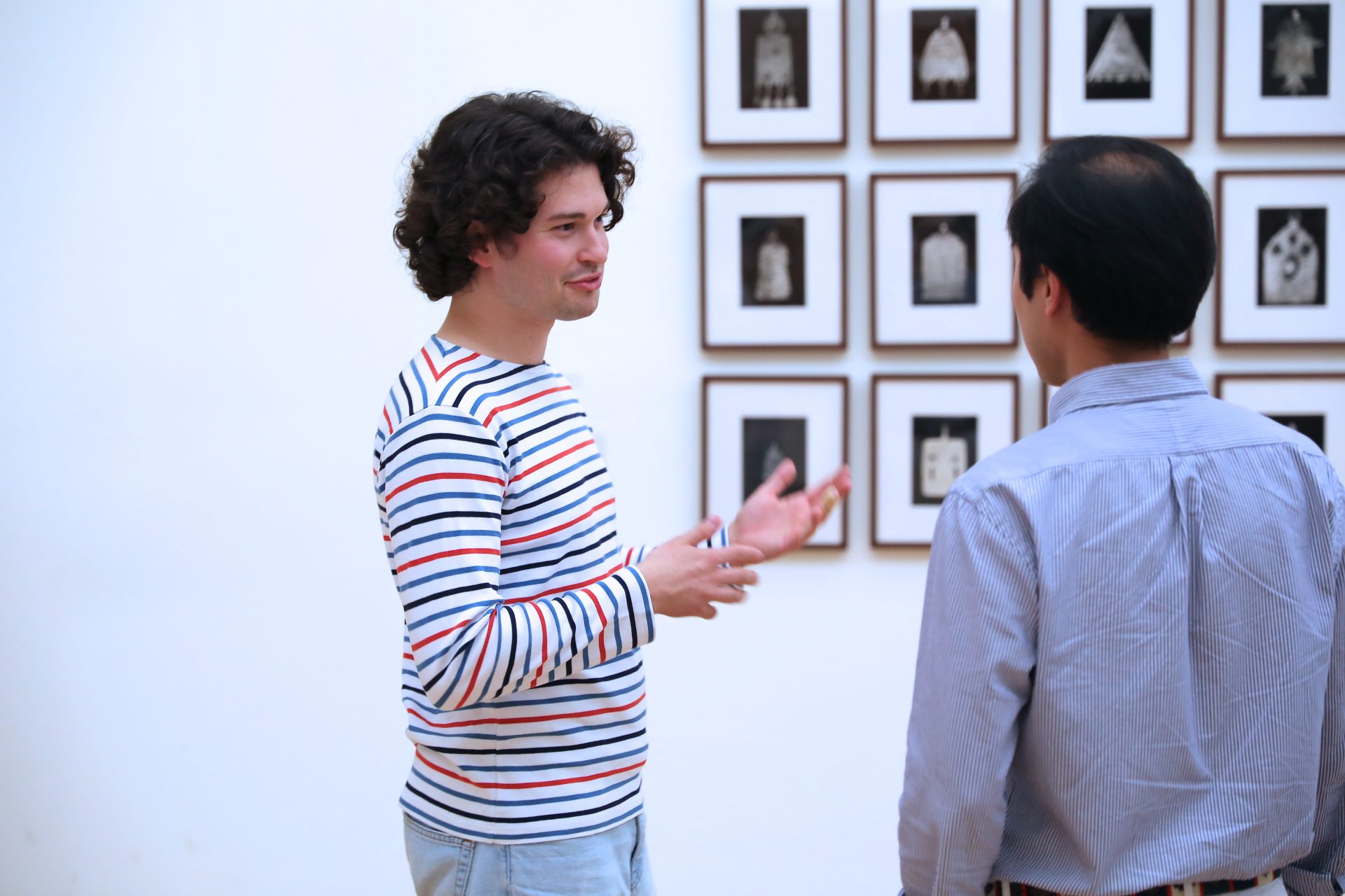 Zwei Personen unterhalten sich vor einer Wand mit gerahmten Kunstwerken in einem modernen Ausstellungsraum.