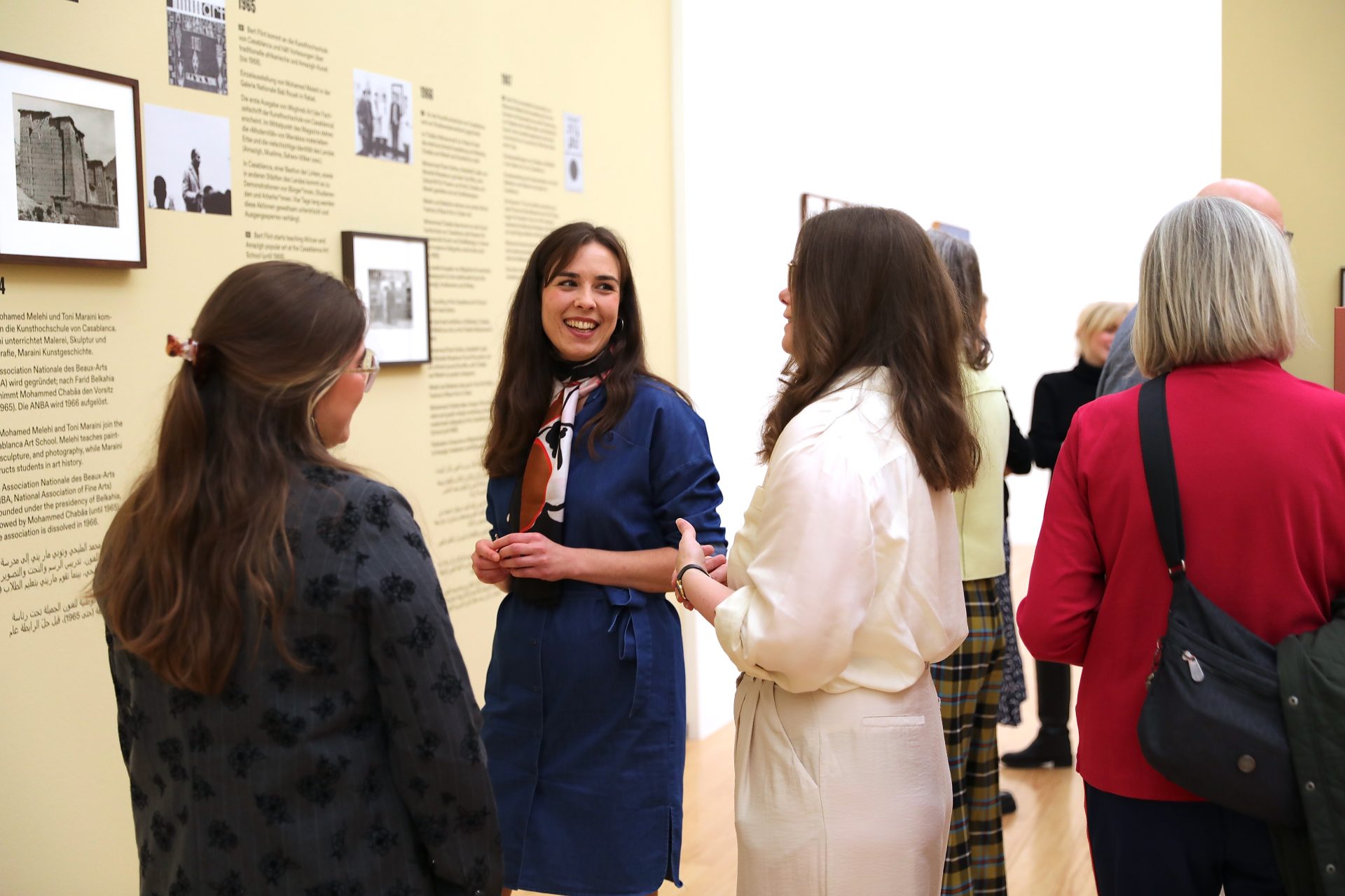 Besucherinnen diskutieren in einem Kunstmuseum vor Wandtexten und Fotografien.