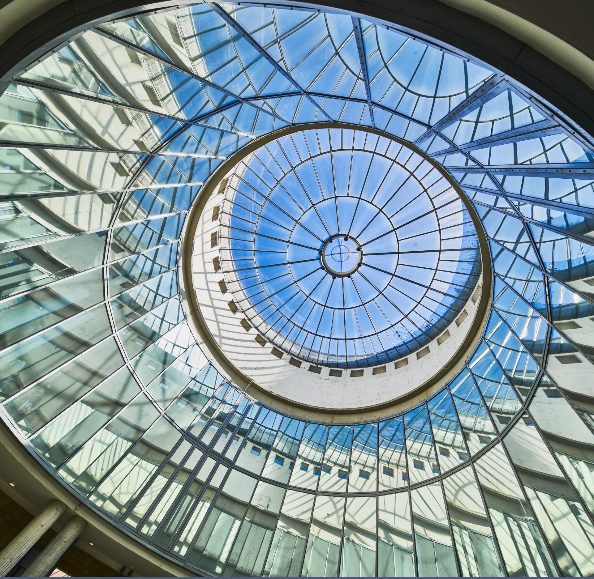 Glasdecke mit kreisförmigem Muster zeigt den Himmel, umgeben von modernen Gebäuden.