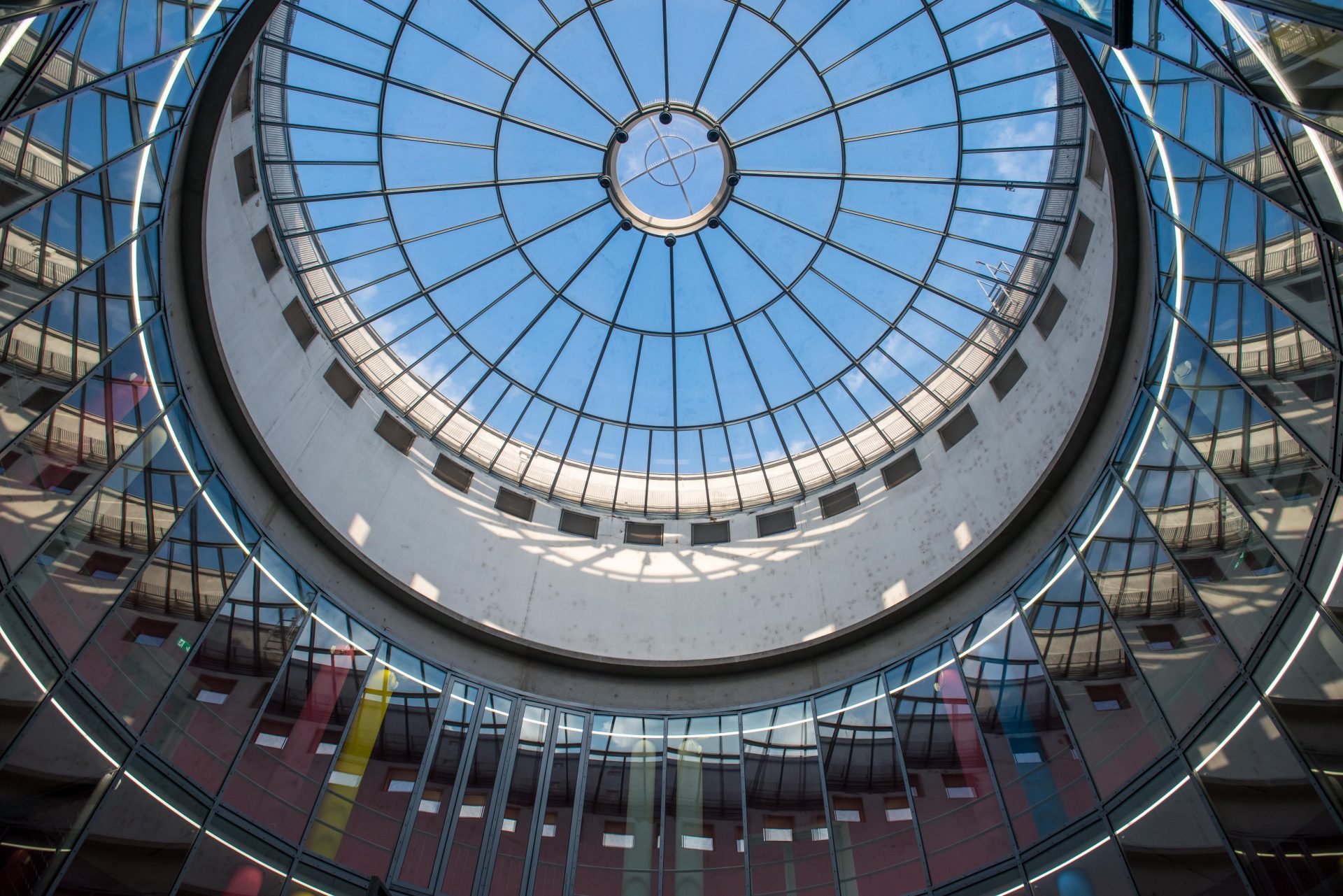 Glasdome mit kreisförmiger Struktur und blauem Himmel, umgeben von modernen Gebäuden.