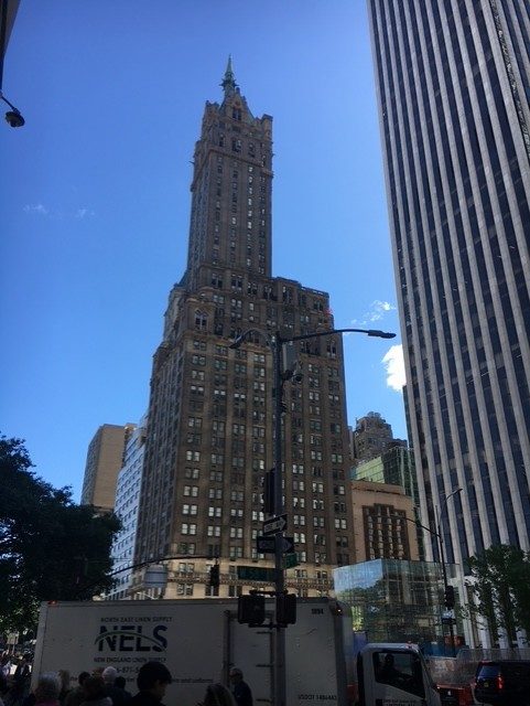 Hohes, historisches Gebäude mit architektonischen Details, umgeben von modernen Wolkenkratzern und klarem Himmel.