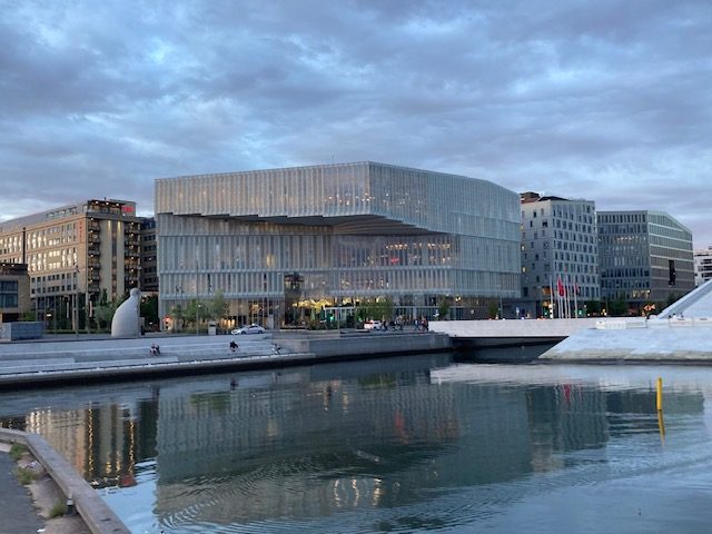 Moderne Architektur eines Wassergebäudes, reflektiert im ruhigen Wasser unter einem bewölkten Himmel.