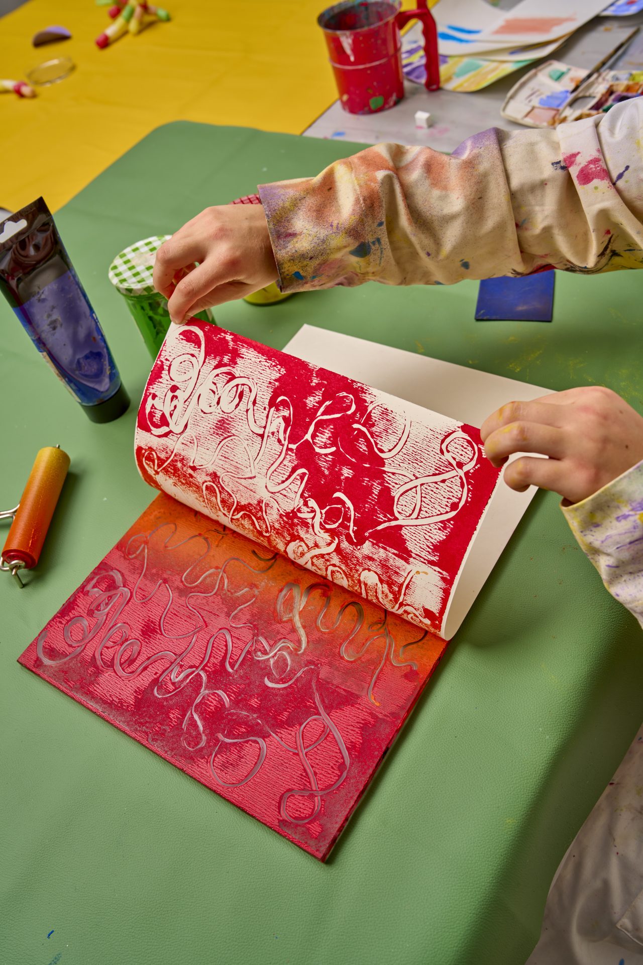 Kreative Hände blättern durch ein buntes Kunstbuch mit roten und orangefarbenen Mustern auf einem Tisch.