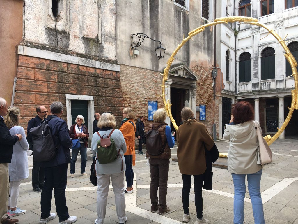 Gruppe von Touristen vor einem alten Gebäude in Venedig, im Hintergrund ein großer, gelber Ring.