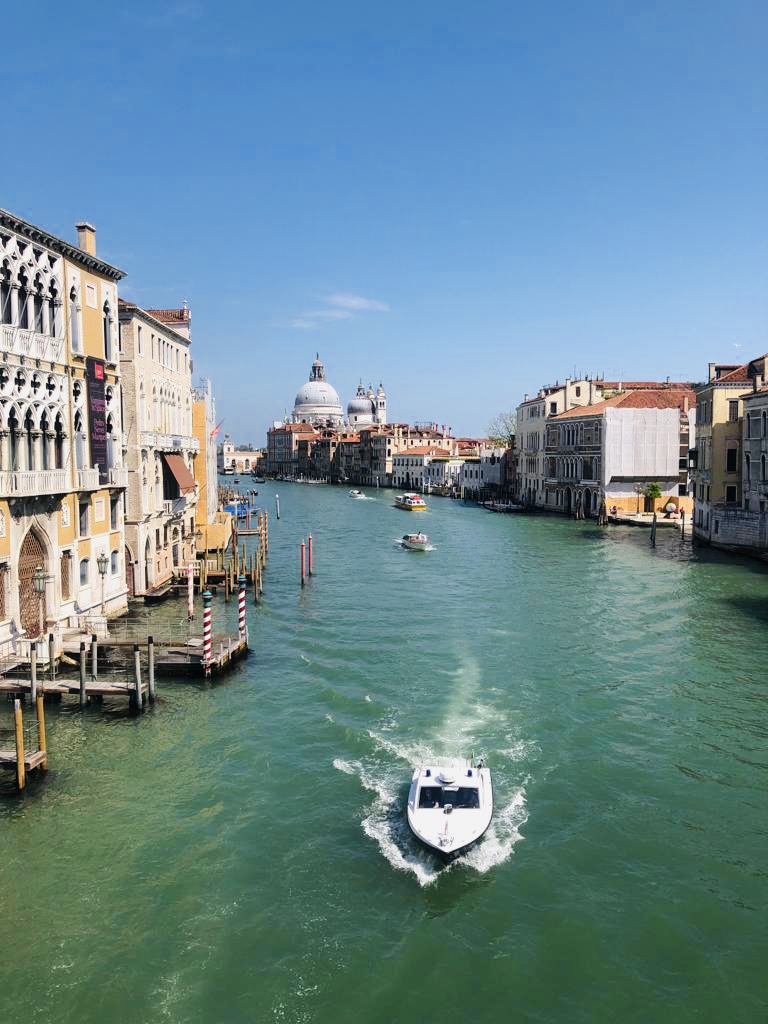 Boote auf einem ruhigen Kanal in Venedig, umgeben von historischen Gebäuden und blauem Himmel.