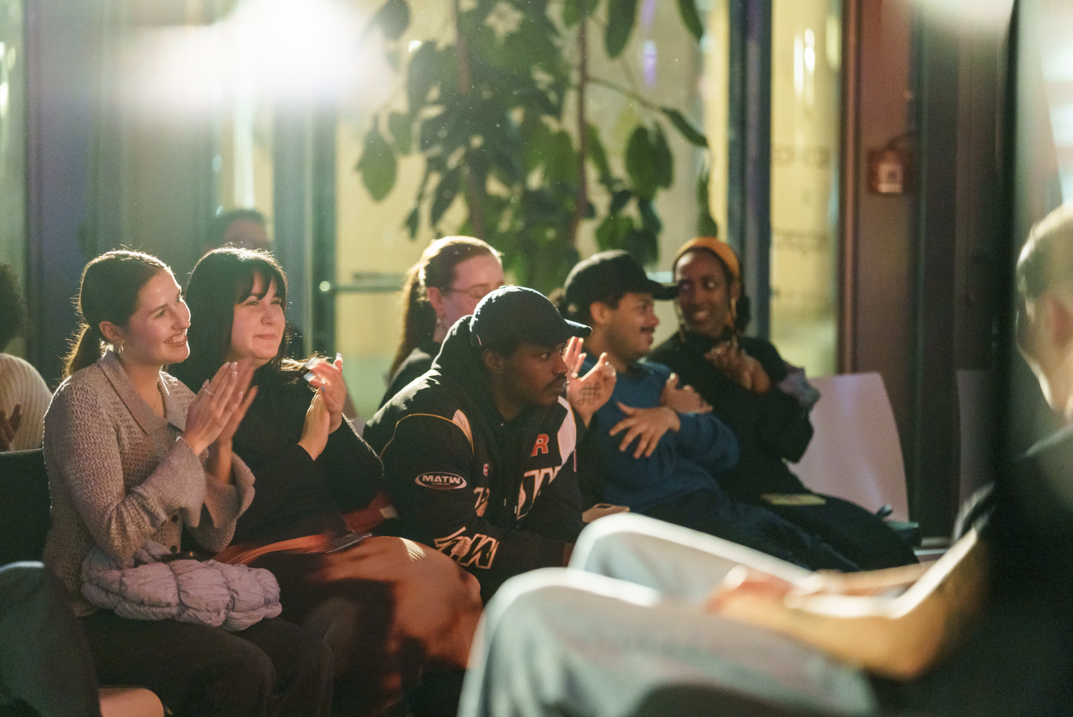 Eine Gruppe von Menschen applaudiert in einem hell erleuchteten Raum während einer Veranstaltung.